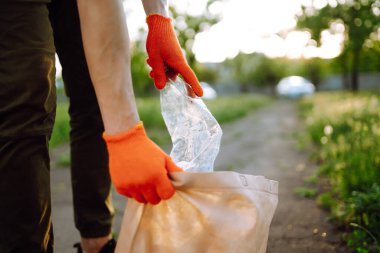 Parkta boş plastik şişeler. Parkta çöp toplama. Koruyucu eldiven giyen erkekler şişe plastiği toplar. Doğayı kurtar.