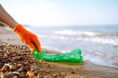 Sahilde çöp. Koruyucu eldiven giyen erkekler deniz sahilinde plastik şişe topluyor. Plastik su şişeleri okyanusta kirleniyor. Doğayı kurtar.