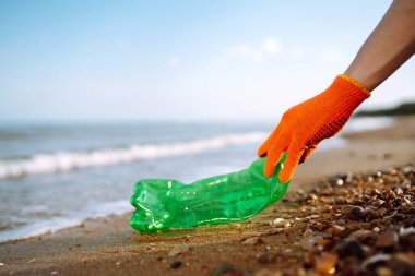 Sahilde çöp. Koruyucu eldiven giyen erkekler deniz sahilinde plastik şişe topluyor. Plastik su şişeleri okyanusta kirleniyor. Doğayı kurtar.
