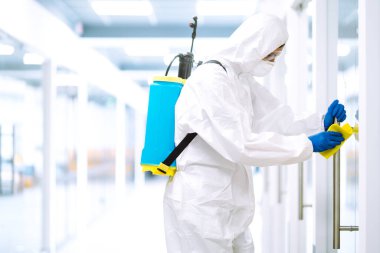Koruyucu kıyafetli bir adam COVID-19 'u önlemek için ofisi yıkıyor. Temizlik ve dezenfekte ofisi mobilyaları.