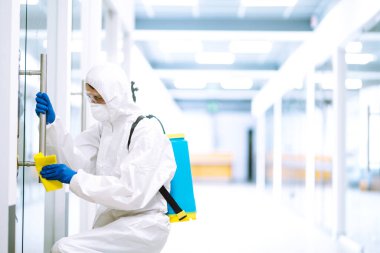 Koruyucu kıyafetli bir adam COVID-19 'u önlemek için ofisi yıkıyor. Temizlik ve dezenfekte ofisi mobilyaları.