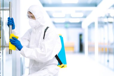 Koruyucu kıyafetli bir adam COVID-19 'u önlemek için ofisi yıkıyor. Temizlik ve dezenfekte ofisi mobilyaları.