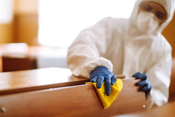 Cleaning and disinfection school class to prevent COVID-19. Man in protective hazmat suit washes school desk  to preventing the spread of coronavirus, pandemic in quarantine city.