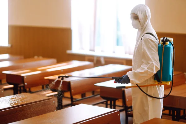 Disinfecting school class to prevent COVID-19. Man in protective hazmat suit with spray chemicals to preventing the spread of coronavirus, pandemic in quarantine city.