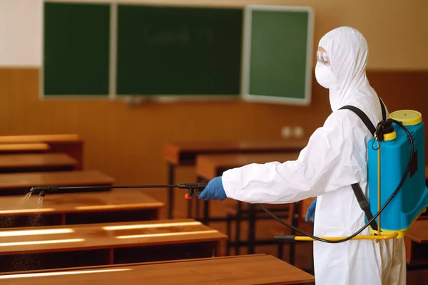 Disinfecting school class to prevent COVID-19. Man in protective hazmat suit with spray chemicals to preventing the spread of coronavirus, pandemic in quarantine city.