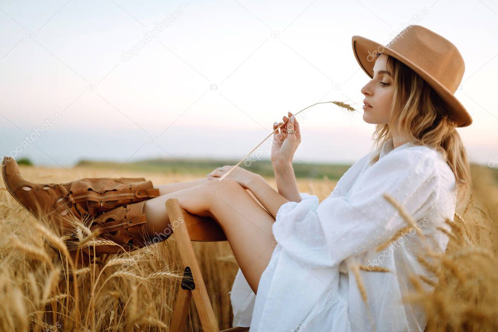 Stylish young girl in a summer white dress and hat posing in a golden wheat field. Fashion, glamour, lifestyle concept.