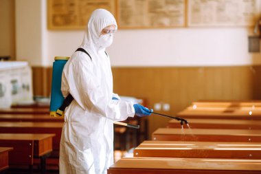 Coronavirüs salgını sırasında okulları dezenfekte etmek. Koruyucu elbise giyen bir adam okulu dezenfekte ediyor. COVID-19.