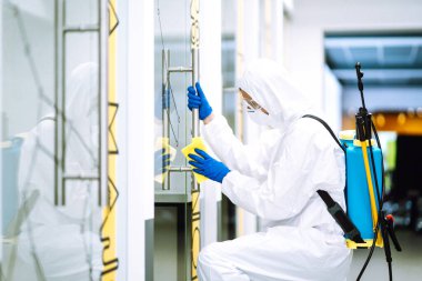 Ofisin temizlenmesi ve dezenfekte edilmesi. Covid-19. Koruyucu takım elbiseli adam ofis mobilyalarını yıkıyor..