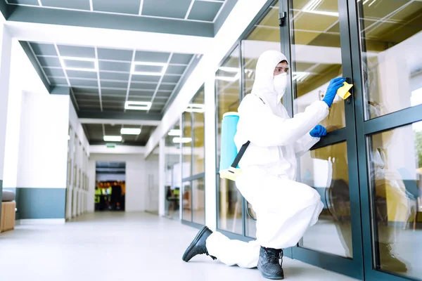 Cleaning and disinfection of office. Covid-19. Man in protective suit washes office furniture.