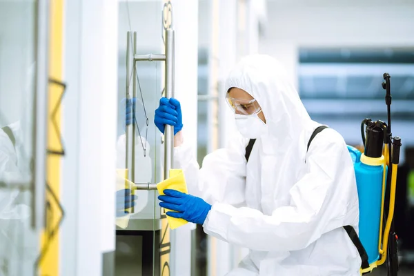 Cleaning and disinfection of office. Covid-19. Man in protective suit washes office furniture.