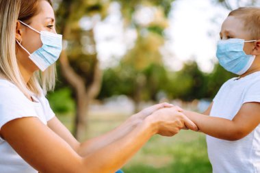 Salgın sırasında parkta maskeli küçük bir çocuk ve anne. Covid 2019.