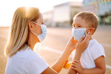 Anne gün batımında salgın sırasında bebek steril tıbbi maskesini takıyor. Karantina şehrinde küçük bir çocuk ve anne tıbbi maske takıyor. Covid 2019.