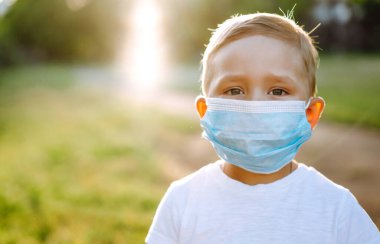Salgın sırasında parkta tıbbi maskeli küçük bir çocuğun portresi. Coronavirus 'tan sağlık ve güvenlik hayatı kavramı. Covid-2019. Çocukların güvenliği.
