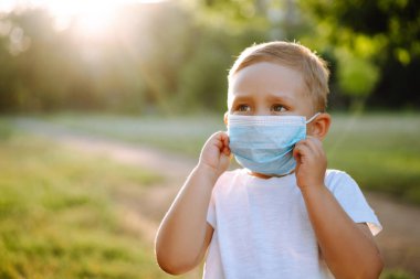 Salgın sırasında parkta tıbbi maskeli küçük bir çocuğun portresi. Coronavirus 'tan sağlık ve güvenlik hayatı kavramı. Covid-2019. Çocukların güvenliği.