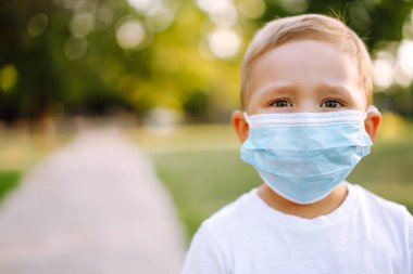Salgın sırasında parkta tıbbi maskeli küçük bir çocuğun portresi. Coronavirus 'tan sağlık ve güvenlik hayatı kavramı. Covid-2019. Çocukların güvenliği.