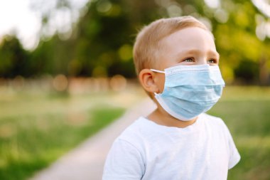 Salgın sırasında parkta tıbbi maskeli küçük bir çocuğun portresi. Coronavirus 'tan sağlık ve güvenlik hayatı kavramı. Covid-2019. Çocukların güvenliği.