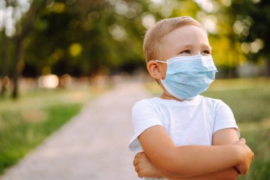 Salgın sırasında parkta tıbbi maskeli küçük bir çocuğun portresi. Coronavirus 'tan sağlık ve güvenlik hayatı kavramı. Covid-2019. Çocukların güvenliği.