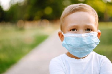 Salgın sırasında parkta tıbbi maskeli küçük bir çocuğun portresi. Coronavirus 'tan sağlık ve güvenlik hayatı kavramı. Covid-2019. Çocukların güvenliği.