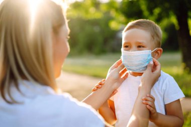 Anne, salgın sırasında parkta bebek steril tıbbi maskesini takıyor. Covid 2019.