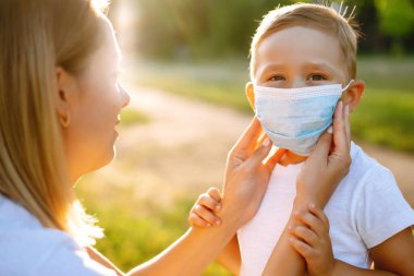 Anne, salgın sırasında parkta bebek steril tıbbi maskesini takıyor. Covid 2019.