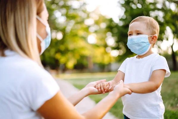 Little boy and mom in medical mask in the park during pandemic. Covid-2019.