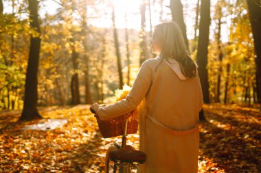 Günbatımında gülen bisikletli genç kız sonbahar ormanında yürüyor..