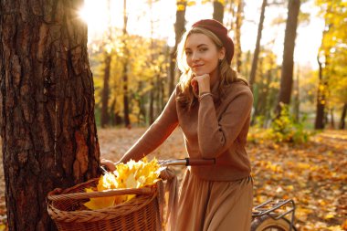 Günbatımında sonbahar ormanında bisiklet süren genç bir kız..