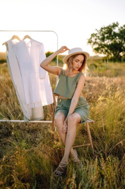 Altın buğday tarlasında güneşli bir günün tadını çıkaran şık bir kız. Yaz elbiseleri altın bir buğday tarlasının arka planında askıda.. 