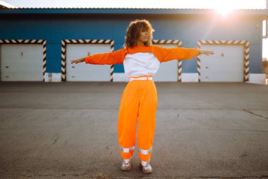 Afrika kökenli Amerikalı bir kız. Gün batımında sokakta dans ediyor. Spor, dans ve şehir kültürü konsepti. Moda yaşam tarzı.