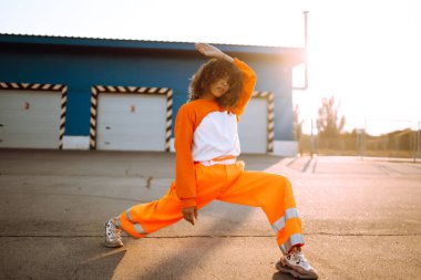 Afrika kökenli Amerikalı bir kız. Gün batımında sokakta dans ediyor. Spor, dans ve şehir kültürü konsepti. Moda yaşam tarzı.