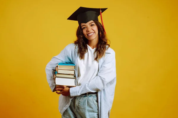 Graduate Girl Graduation Hat Her Head Books Stands Yellow Background — Stock Photo, Image