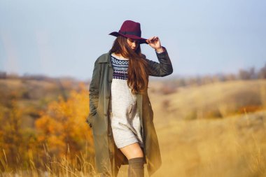 Sonbahar parkında şapkalı zarif bir kadın yürüyor. Çayırda sonbahar havasının tadını çıkaran şık bir kadın. Sonbahar modası. Dinlenme, rahatlama, yaşam tarzı konsepti.