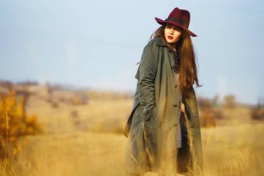 Sonbahar parkında şapkalı zarif bir kadın yürüyor. Çayırda sonbahar havasının tadını çıkaran şık bir kadın. Sonbahar modası. Dinlenme, rahatlama, yaşam tarzı konsepti.