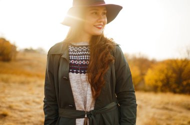 Sonbahar parkında şapkalı zarif bir kadın yürüyor. Çayırda sonbahar havasının tadını çıkaran şık bir kadın. Sonbahar modası. Dinlenme, rahatlama, yaşam tarzı konsepti.