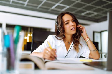 Genç kız öğrenci internetten kablosuz kulaklık dersi alıyor. Dil öğreniyor. Ders dinliyor. Webinar 'ın not yazışını izliyor. Ncov durumu sırasında video çağrısı