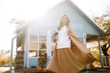 Sonbaharda mavi bir evin arka planında retro kamerası olan şık bir kadın. Eğleniyor ve gülüyor. Sonbahar yaşam tarzı.