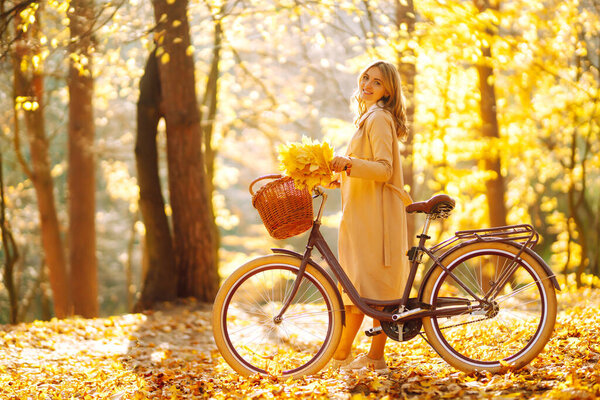 Стильная женщина с велосипедом наслаждается осенней погодой в парке. Женщина, гуляющая в осеннем лесу.