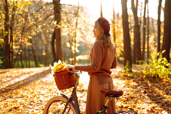 Стильная женщина с велосипедом наслаждается осенней погодой в парке. Женщина, гуляющая в осеннем лесу.