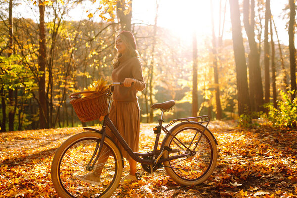 Стильная женщина с велосипедом наслаждается осенней погодой в парке. Женщина, гуляющая в осеннем лесу.