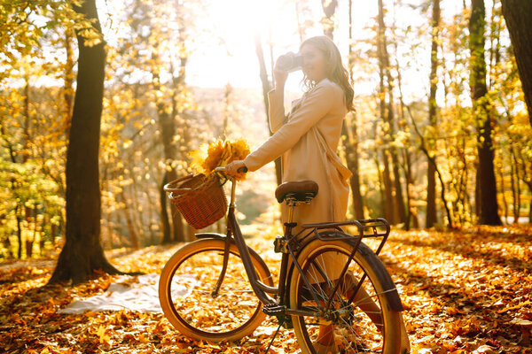 Стильная женщина с ретро-камерой наслаждается осенней погодой на закате в парке. Она веселится и смеется. Осенний образ жизни.