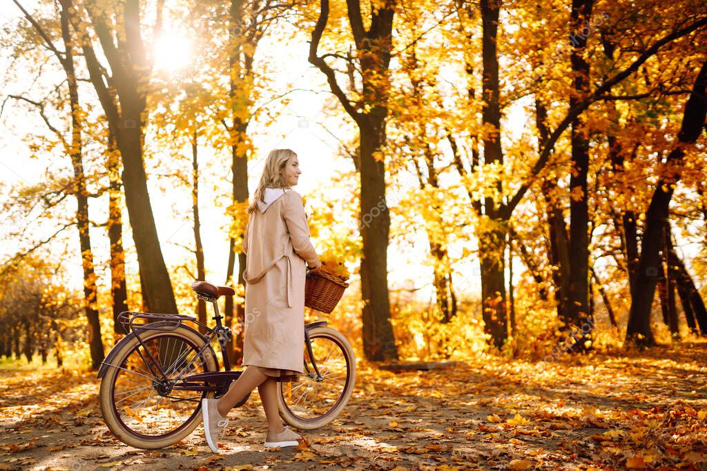 Stylish woman with a bicycle enjoying autumn weather in the park. Beautiful Woman walking  in the autumn forest.