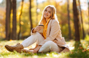 Güz parkında kahve içen güzel kadın. Rahatlama, keyif alma, doğayla baş başa kalma..