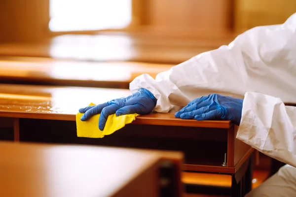 Hand in gloves are cleaning school class to prevent COVID-19. Disinfecting schools during coronavirus pandemic.