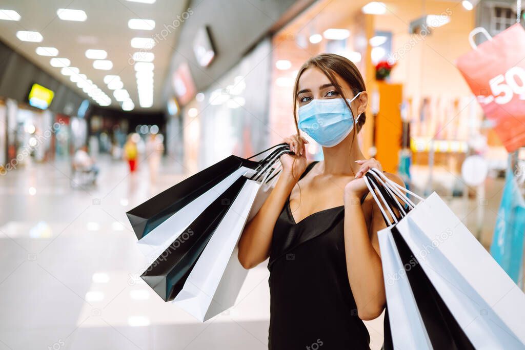 Woman in shopping. Young woman in protective sterile medical mask on her face with shopping bags in the mall. Purchases, black friday, discounts,  sale concept. Covid-2019.