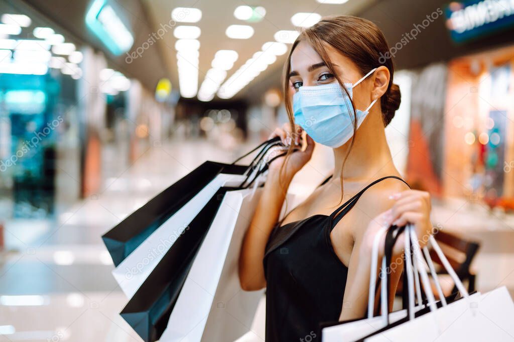 Woman in shopping. Young woman in protective sterile medical mask on her face with shopping bags in the mall. Purchases, black friday, discounts,  sale concept. Covid-2019.