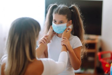Annesi kızına steril tıbbi maske takıyor. Virüs enfeksiyonundan, salgından ve karantinada salgın hastalıklardan koruyor. Covid-19 salgını sırasında yaşam.