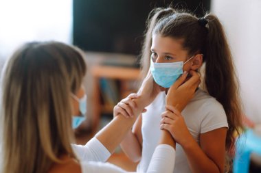 Annesi kızına steril tıbbi maske takıyor. Virüs enfeksiyonundan, salgından ve karantinada salgın hastalıklardan koruyor. Covid-19 salgını sırasında yaşam.