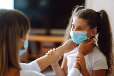Annesi kızına steril tıbbi maske takıyor. Virüs enfeksiyonundan, salgından ve karantinada salgın hastalıklardan koruyor. Covid-19 salgını sırasında yaşam.