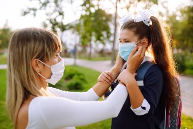 Gün batımında covid-19 sırasında tıbbi maske takan küçük bir kız ve anne. Annesi kızına steril tıbbi maske takıyor. Virüs enfeksiyonundan, salgından ve karantinada salgın hastalıklardan koruyor.. 