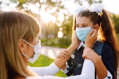 Gün batımında covid-19 sırasında tıbbi maske takan küçük bir kız ve anne. Annesi kızına steril tıbbi maske takıyor. Virüs enfeksiyonundan, salgından ve karantinada salgın hastalıklardan koruyor.. 